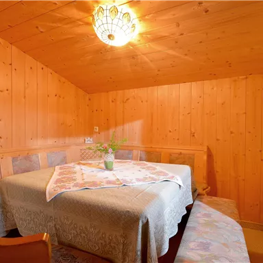 Ein gemütlicher Essbereich mit Holzverkleidung und einem runden Tisch. Eine schöne Lampe beleuchtet den Raum, und ein Blumenarrangement steht in der Mitte des Tisches.