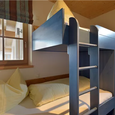 Ein gemütliches Schlafzimmer mit einem Etagenbett und schönen Kissen. Das Zimmer hat große Fenster und ist hell und einladend.