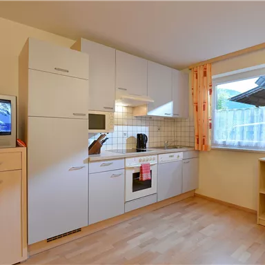 A modern kitchen with bright furniture and a wooden floor. Windows with curtains let in natural light.