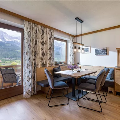 Ein einladender Essbereich mit einem Tisch und Stühlen, umgeben von großen Fenstern mit Blick auf die Berge. Die Einrichtung ist modern und gemütlich, mit warmen Holztönen und einer angenehmen Atmosphäre.