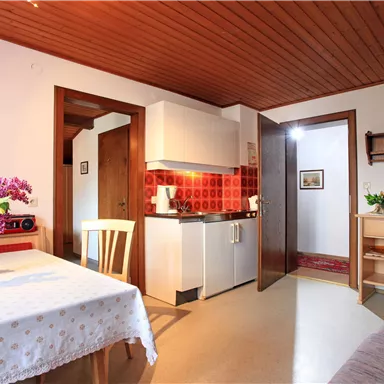 A cozy apartment with a small kitchen and a dining area. On the table sits a vase with colorful flowers.