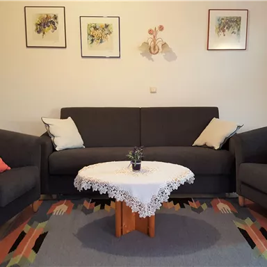 A cozy living room with a gray sofa and two armchairs. Table with a white tablecloth and a plant in the center.