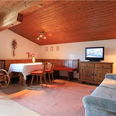 A cozy living room with a wooden ceiling and a carpet. There is a dining room, a couch, and a television.