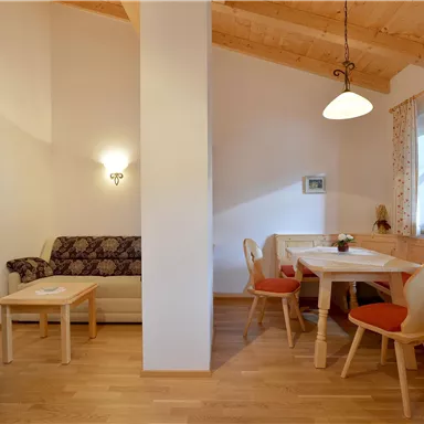 A cozy living area with a wooden ceiling and table group. A sofa and chairs create an inviting atmosphere.
