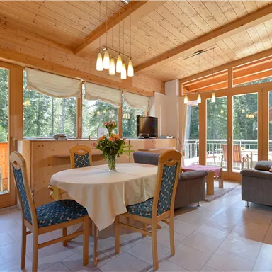 Bright and modern living room with large windows and a view of greenery. A round dining table and comfortable seating invite you to relax.