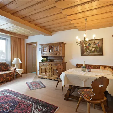 A cozy living room with a wooden ceiling and rustic furniture. A round table and elegant decoration create an inviting atmosphere.