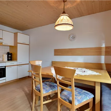 A bright kitchen with a wooden dining area and chairs. The kitchen is modernly furnished and features an electric stove as well as a cozy atmosphere.