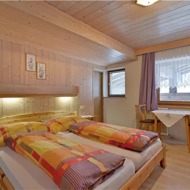 A cozy bedroom with wooden walls and a double bed. There are two windows that let in plenty of light, as well as a small sitting area.
