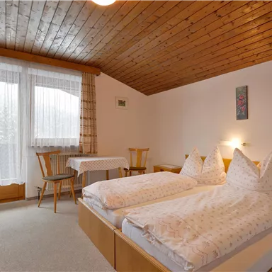 A cozy bedroom with two separate beds and wooden paneling. Large windows let in plenty of light and provide a view of the exterior.