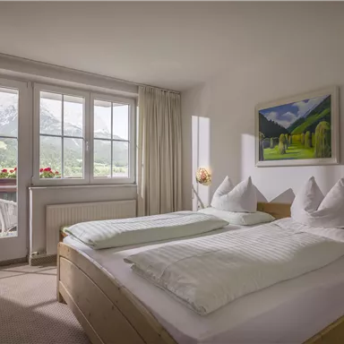 Ein gemütliches Schlafzimmer mit zwei Betten und Blick auf die Berge. Große Fenster sorgen für viel Tageslicht und eine angenehme Atmosphäre.