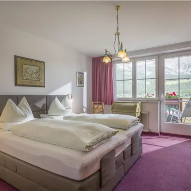 Ein gemütliches Hotelzimmer mit zwei Betten und warmen Farben. Große Fenster bieten Blick auf die umliegende Landschaft.