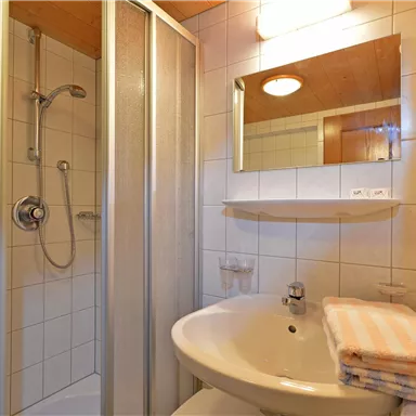 Ein modernes Badezimmer mit einer Duschkabine und einem Waschbecken. Handtücher liegen ordentlich daneben.