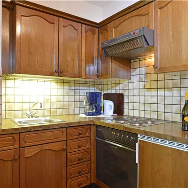 A modern kitchen with wooden cabinets, sink, and kitchen appliances. On the countertop are a kettle, a bottle of wine, and glasses.