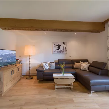 Ein modernes Wohnzimmer mit einer gemütlichen Couch und einem Fernseher. Der Raum ist hell und einladend, mit Holz- und Textildekoren.
