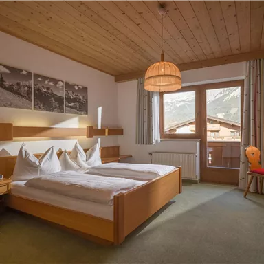 A bright hotel room with a double bed and modern furnishings. The large windows offer a view of the mountains and create a pleasant atmosphere.