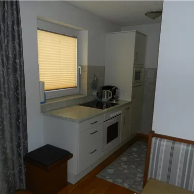 Eine moderne Küche mit weißen Schränken und einer Küchenzeile. Das Fenster hat einen Jalousien und es gibt einen kleinen Tisch im Raum.