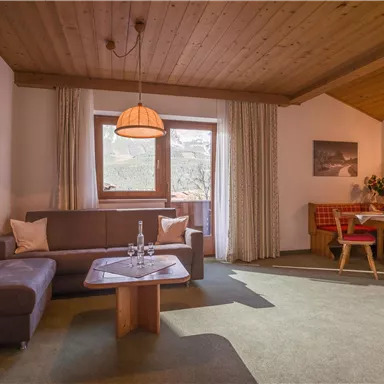 A cozy living room with a wooden ceiling, a sofa, and a table. Large windows provide plenty of daylight, and the dining area invites you to linger.