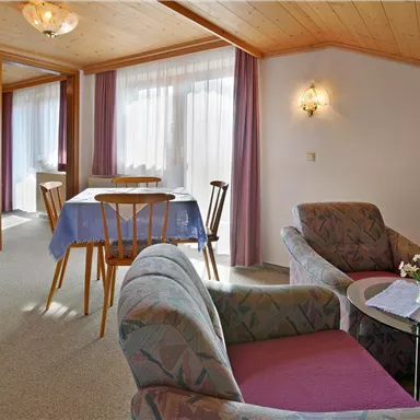 Ein gemütliches Wohnzimmer mit einem Essbereich und einem Fernseher. Große Fenster lassen viel Licht herein und sorgen für eine einladende Atmosphäre.