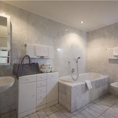 Ein modernes Badezimmer mit marmorierten Wänden und eleganter Ausstattung. Es gibt eine Badewanne, ein Waschbecken und passende Handtücher.