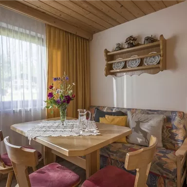 A cozy dining area with a wooden table and chairs. A flower vase is on the table, and the room is bright and cheerfully decorated.