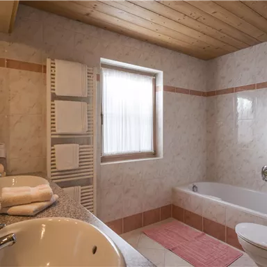A modern bathroom with a bathtub, two sinks, and a wooden ceiling. There are also towels and heating in the room.