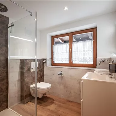 A modern bathroom with a glass shower and a white sink. Large windows let in plenty of light.