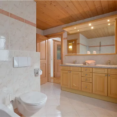 A modern bathroom with a wooden ceiling and bright tiles. There is a shower, a toilet, and a large mirror above the sink.