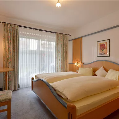 A cozy bedroom with two beds and soft pillows. Large windows provide plenty of daylight, and the decor is modern and inviting.