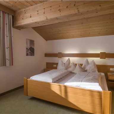 A cozy bedroom with a wooden ceiling and two single beds. The room is bright and friendly with a window and modern furniture.
