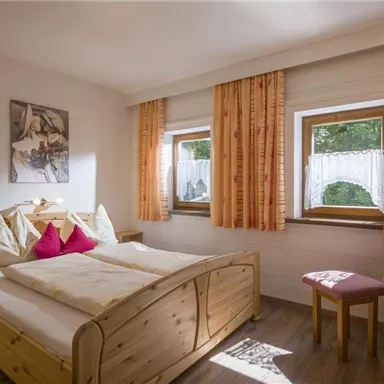 A cozy bedroom with a large bed and colorful pillows.
Bright curtains let in plenty of light and a small flower vase creates a friendly atmosphere.