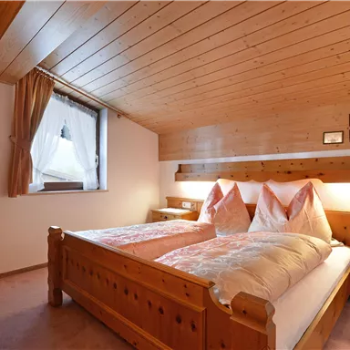 A cozy bedroom with wood-paneled walls and a double bed. The windows let in natural light and create a warm atmosphere.