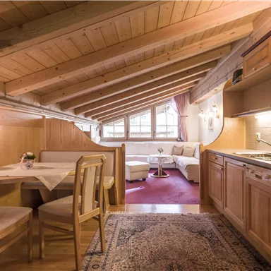 A cozy kitchen with wooden details and a dining table. The light-flooded living room is furnished with comfortable furniture.