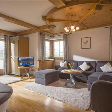 A cozy living room with a comfortable sofa and a small table. Large windows let in plenty of daylight and offer a view outside.