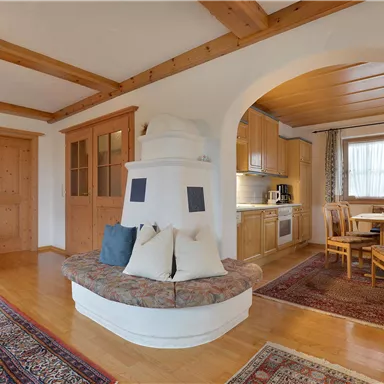 A cozy living room with wooden beam ceiling and a bright dining area. The room is well-lit and offers an inviting atmosphere.
