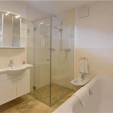 Ein modernes Badezimmer mit einer Badewanne und einer Glasdusche. Es gibt einen eleganten Waschtisch und viel Licht.