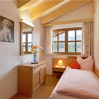 Ein gemütliches Schlafzimmer mit Holzdecke und großen Fenstern. Es gibt einen Schreibtisch, einen Stuhl und eine Dekoration mit Blumen und einem Bild an der Wand.