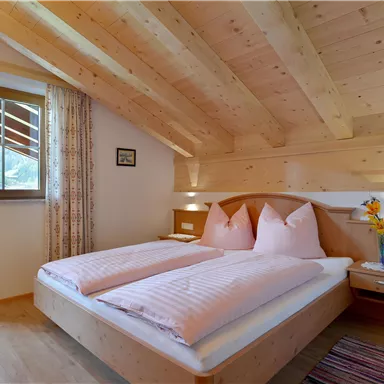Ein gemütliches Schlafzimmer mit hellen Holzwänden und einem großen Fenster. Das Zimmer ist mit einem Doppelbett und einem Nachttisch dekoriert.
