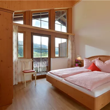 Ein gemütliches Schlafzimmer mit Holzverkleidung und großen Fenstern. Es verfügt über ein Doppelbett und einen TV, mit Blick auf die umliegende Landschaft.