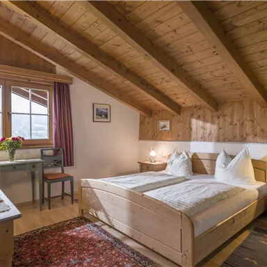 Ein gemütliches Schlafzimmer mit Holzdecken und einem Doppelbett. Es gibt einen Schreibtisch, einen Fernseher und große Fenster mit Blick nach draußen.