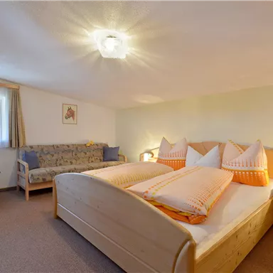 A cozy bedroom with a large bed and two seating areas. The walls are painted light, and the light is warm and inviting.
