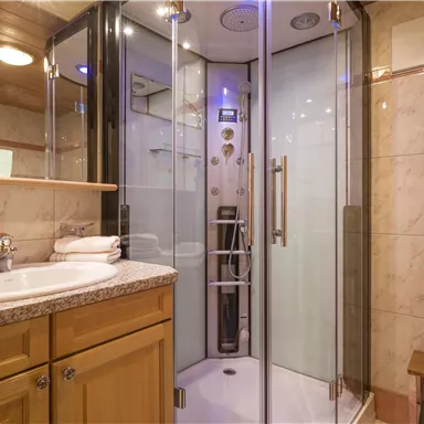 A modern bathroom with a glass shower and light wood paneling. The sink is made of granite and offers fresh towels.
