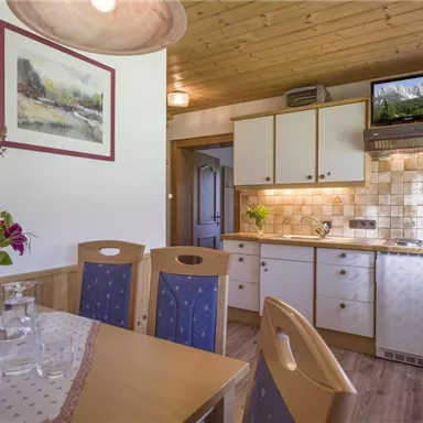 A cozy kitchen with a dining table and chairs. The walls are bright, and there are fresh flowers as well as modern kitchen elements.