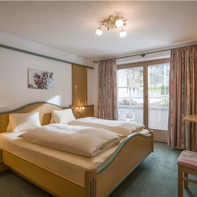 A cozy bedroom with two beds, a desk, and a window with a view outside. The décor is bright and inviting.