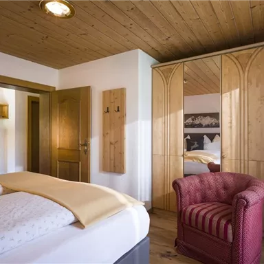 A cozy bedroom with a large bed and a red armchair. The room features wooden ceilings and stylish furniture.