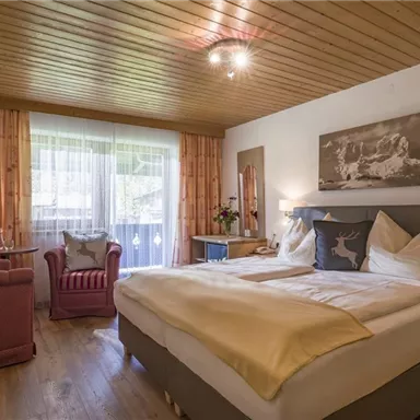A cozy bedroom with a wooden ceiling and a large bed. The room has a red armchair, a television, and plenty of daylight.