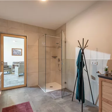 A modern bathroom with a glass shower and wooden shelves. The bright furnishings create an inviting atmosphere.