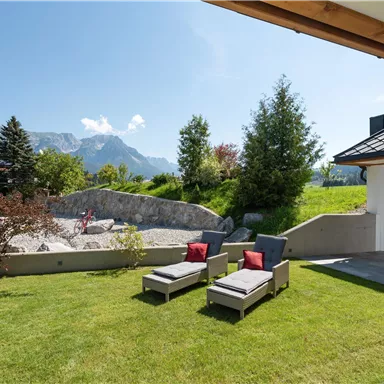 A beautiful garden with sun loungers and a view of the mountains. The sky is clear and sunny.