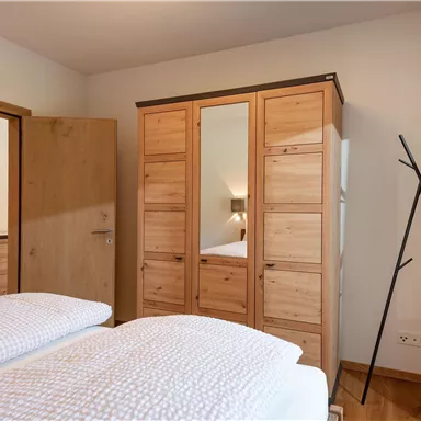 A cozy bedroom with two single beds and a wooden wardrobe. The walls are light, and there is a modern clothes rack.