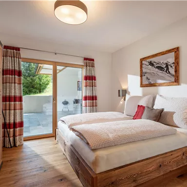A cozy bedroom with a double bed and wooden furniture. Large windows provide plenty of light and a view of nature.