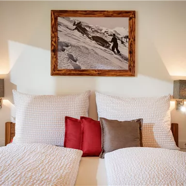 An inviting bedroom with two beds and cozy pillows. A beautiful picture of a snow landscape hangs on the wall.